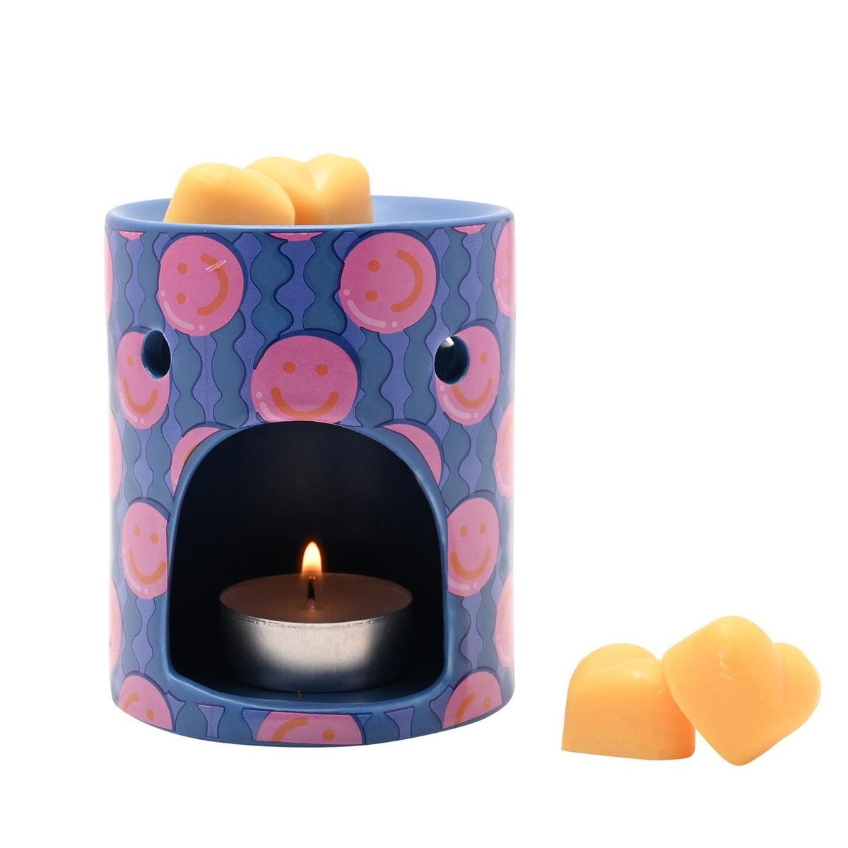 Round blue ceramic wax melt burner with pink smiley face pattern, lit tealight in the front opening and orange wax melts in the top dish, shown with extra melts beside it on a white background.