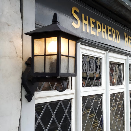 A black Winchester 1 Light Outdoor Wall Up Light enhances the building with diamond-patterned windows, while the sign above subtly suggests the name Shepherd Neame. Historical elegance is perfectly captured as the tranquil street mirrors in the glass.