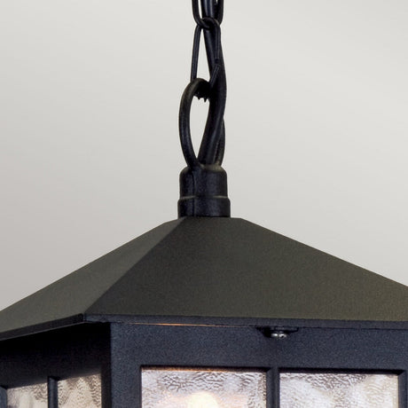 Close-up of the Winchester 1 Light Outdoor Chain Pendant in black, showcasing its vintage design with a metal lantern and textured glass, elegantly suspended by a twisted chain. This charming fixture adds character against the neutral, light gray background.