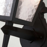 The York 1 Light Outdoor Wall Up Light – Black features a close-up view of its exquisite design, showcasing a black metal wall mount complemented by textured glass panels. The lighting softly reflects off the glass, accentuating its wavy pattern. This weather-resistant fixture is secured to a decorative black metal backplate, imparting vintage-inspired charm.