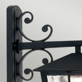 Close-up of the Canterbury Outdoor Wall Lantern Down in black, mounted on a wall. This traditional lighting piece showcases decorative scrollwork and a glass enclosure, offering a classic and elegant appearance. Crafted from durable die-cast aluminum, it promises lasting beauty in any setting.