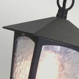 A close-up of the York 1 Light Outdoor Chain Light in black highlights its textured glass panels, which emit a warm glow. This lantern, featuring a pointed top and vintage design, hangs elegantly from a loop against a smooth, light gray background—ideal for enhancing outdoor lighting ambiance.