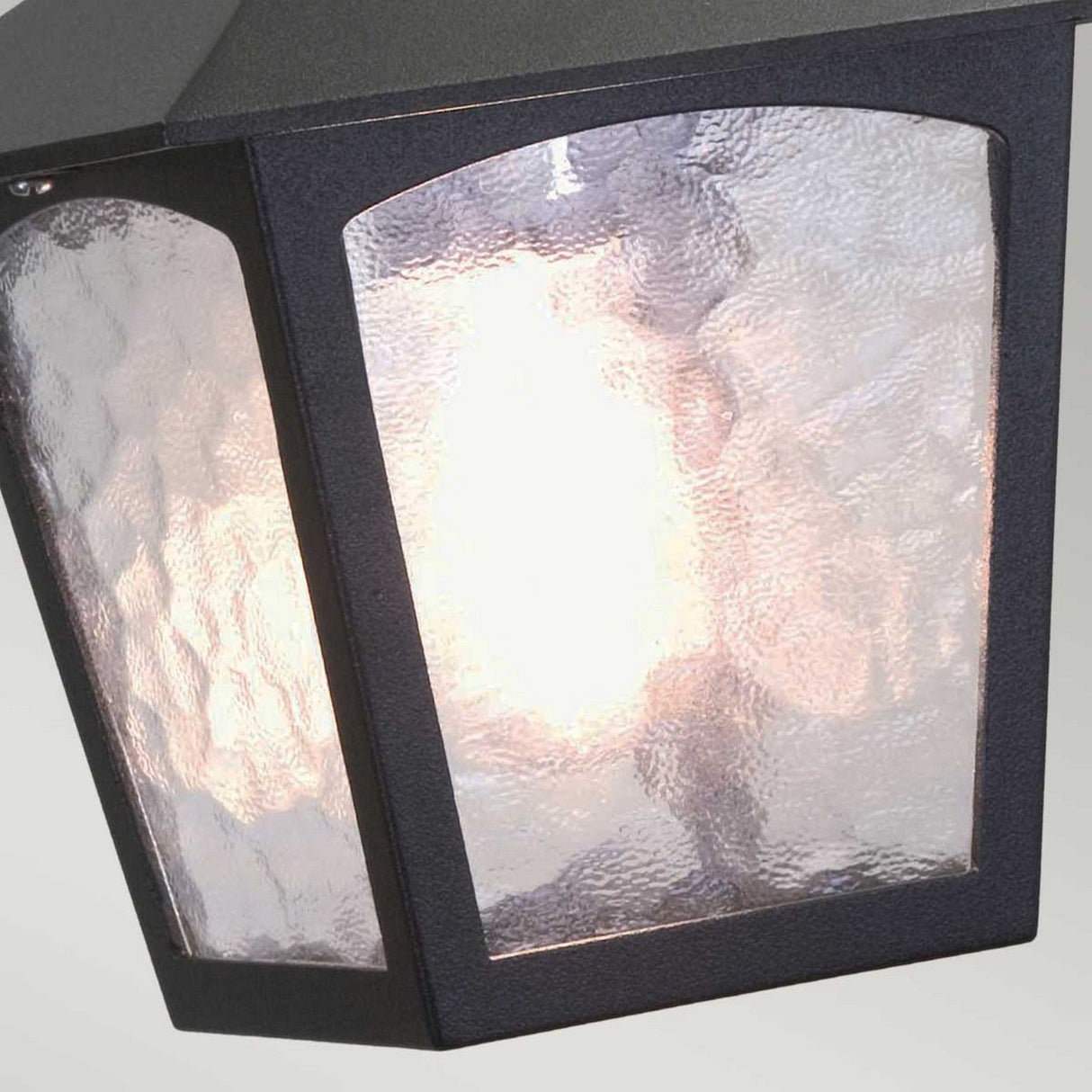 A close-up of the York 1 Light Outdoor Chain Light in black, featuring a textured glass pane and lit from within. This design showcases a classic, slightly arched frame that emits a warm glow, enhancing its vintage aesthetic while soft ambient light diffuses through the glass.