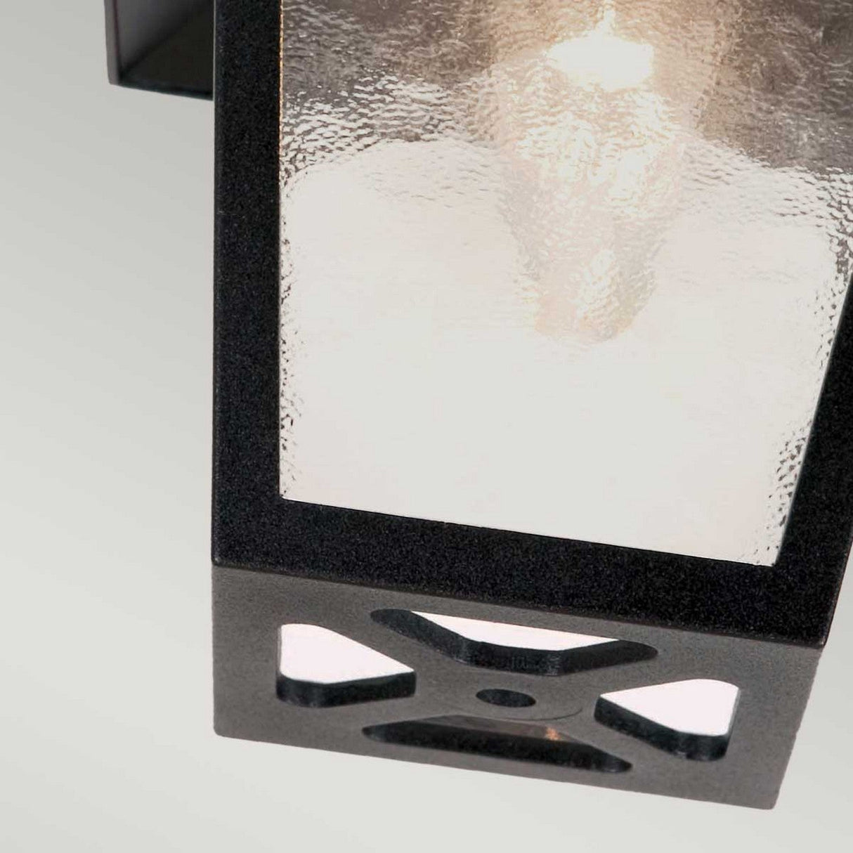 Detailed view of the York 1 Light Outdoor Flush Porch Light, featuring a black metal frame and frosted glass panels that house a gently glowing E27 bulb. The design boasts a rectangular shape with a crisscross pattern at the base, constructed from durable die-cast aluminum.