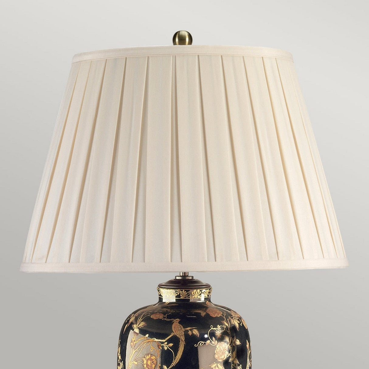 Introducing the Black Birds Table Lamp - Black & Gold, featuring a classic pleated cream-colored shade that highlights traditional Chinese craftsmanship. The lamp's ornate base showcases intricate floral designs and a stunning gold birds pattern on a dark background. Finished with a metal finial, this piece exudes elegance and charm.