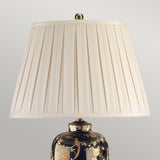 Introducing the Black Birds Table Lamp - Black & Gold, featuring a classic pleated cream-colored shade that highlights traditional Chinese craftsmanship. The lamp's ornate base showcases intricate floral designs and a stunning gold birds pattern on a dark background. Finished with a metal finial, this piece exudes elegance and charm.