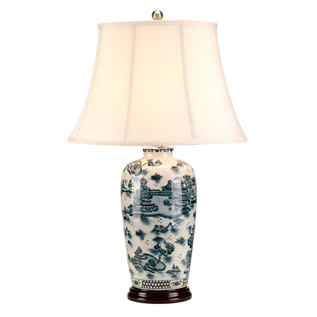 The Blue Traditional Table Lamp - Blue & White showcases a decorative design with a white, tapered lampshade and a ceramic base adorned with blue and white traditional Asian-style landscape patterns reminiscent of Chinese porcelain, all supported by an elegant dark circular wooden stand.