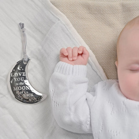 Silverplated crescent moon plaque with grey ribbon, engraved "Love You to the Moon & Back," shown beside a sleeping baby's hand on a white blanket.