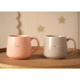Pink "mummy" and grey "daddy" porcelain mugs with silver lettering, star and moon detail, and curved handles, set on a wooden table against a star-patterned wall.