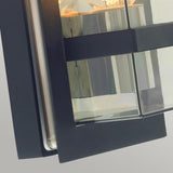 A close-up of the Boden Outdoor 1 Light Wall Light, featuring a sleek Art Deco design with a black metal frame and clear glass panels. The light is switched on, casting a warm glow through the transparent sections, ideal for outdoor use thanks to its IP54 rating.