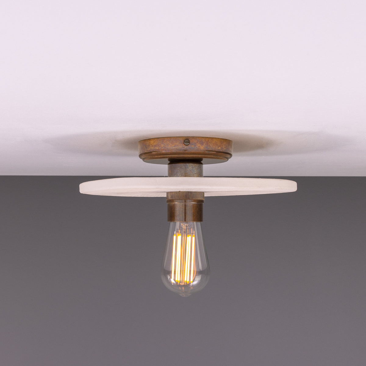 Bog Oak ceramic ceiling light with a flat round matt white striped disc and brass lampholder holding a bare bulb, shown against a plain background.