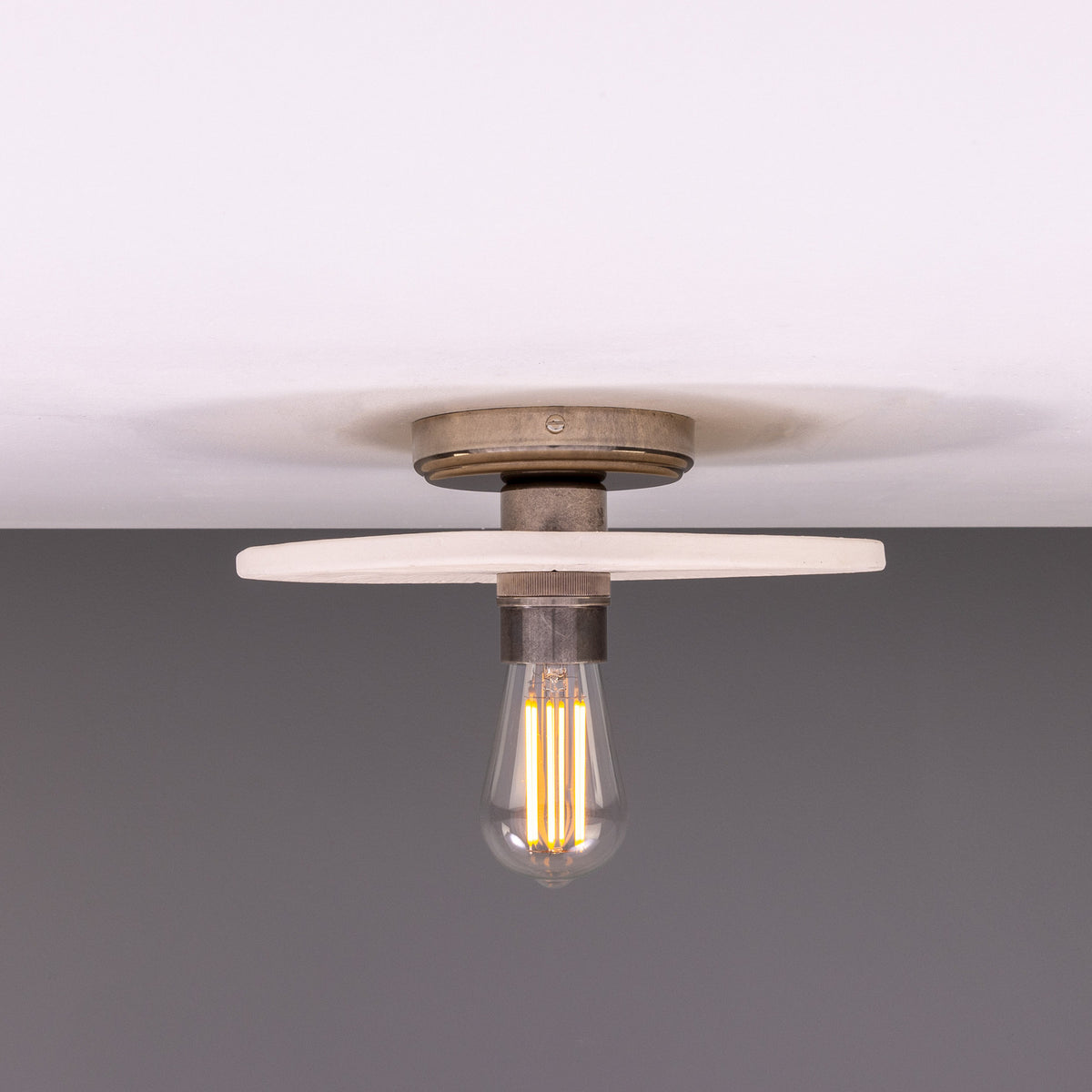 Bog Oak ceramic ceiling light with a flat round matt white striped disc and brass fitting, holding a single exposed bulb, shown against a plain background.