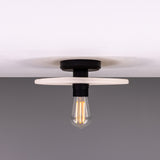 Bog Oak ceramic ceiling light with a flat round disc in matt white striped glaze, black lampholder and exposed bulb, shown against a plain grey background.