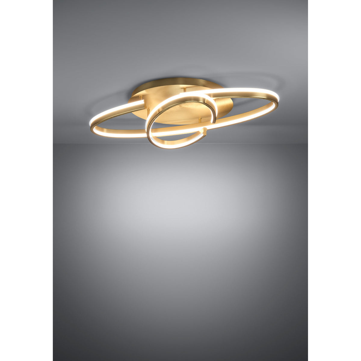 Bogado LED flush ceiling light in gold, featuring an oval ring and smaller round loop in steel with a glowing white diffuser, mounted on a round ceiling plate against a grey background.