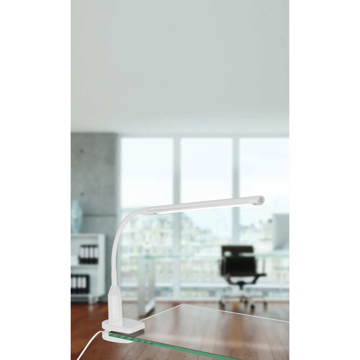 Bolbanne Clamp Lamp in white plastic, slim LED bar head on a flexible gooseneck, clamped to a glass desk edge in a bright office setting with a chair and window in the background.