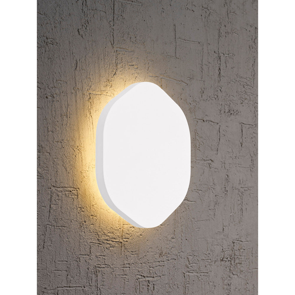 Bora 18cm hexagonal LED wall light in matt white, mounted on a textured grey wall with warm 3000K backlight glow around the diffuser.