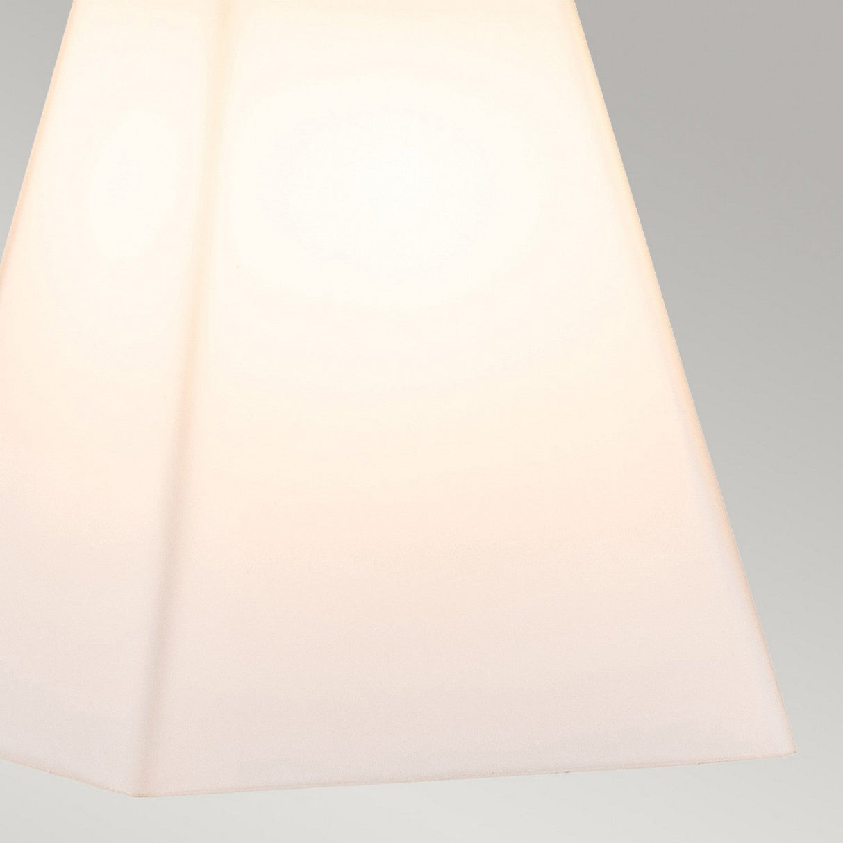 A close-up of a minimalist, white, pyramid-shaped lampshade softly illuminated against a neutral gray backdrop, showcasing the elegance of opal glass shades as seen in the Bowtie 2 Light Wall Light in Matte Black.