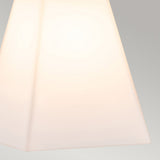 A close-up of a minimalist, white, pyramid-shaped lampshade softly illuminated against a neutral gray backdrop, showcasing the elegance of opal glass shades as seen in the Bowtie 2 Light Wall Light in Matte Black.