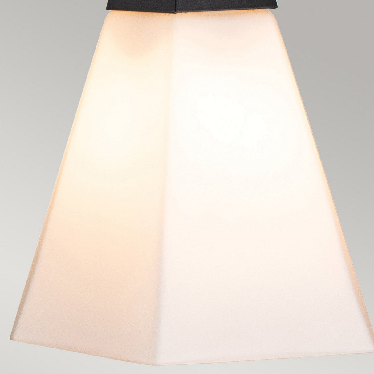 A close-up of the Bowtie 3 Light Wall Light in matte black showcases its modern, geometric design with a frosted white lampshade. Positioned centrally against a neutral gray background, it emanates an elegant, soft glow.