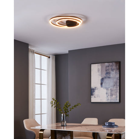 Brasmane LED Flush Ceiling Light in black, featuring two off-centre aluminium and steel rings with white diffusers, shown illuminated on a dining room ceiling above a marble table.