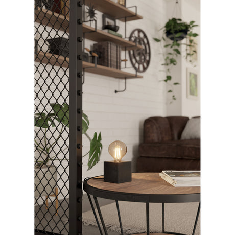 Bremessa Table Lamp in black, a compact wooden cube base with bare E27 bulb on top, shown on a coffee table in a living room setting.