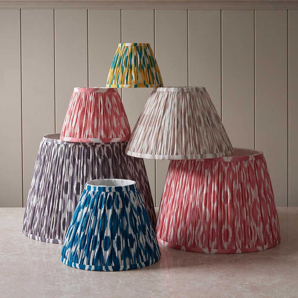 Endon Brenwell tapered lamp shades in ikat-printed pleated faux silk, grouped in coral pink, pearl grey, marlin blue and yellow-jade against panelled wall.
