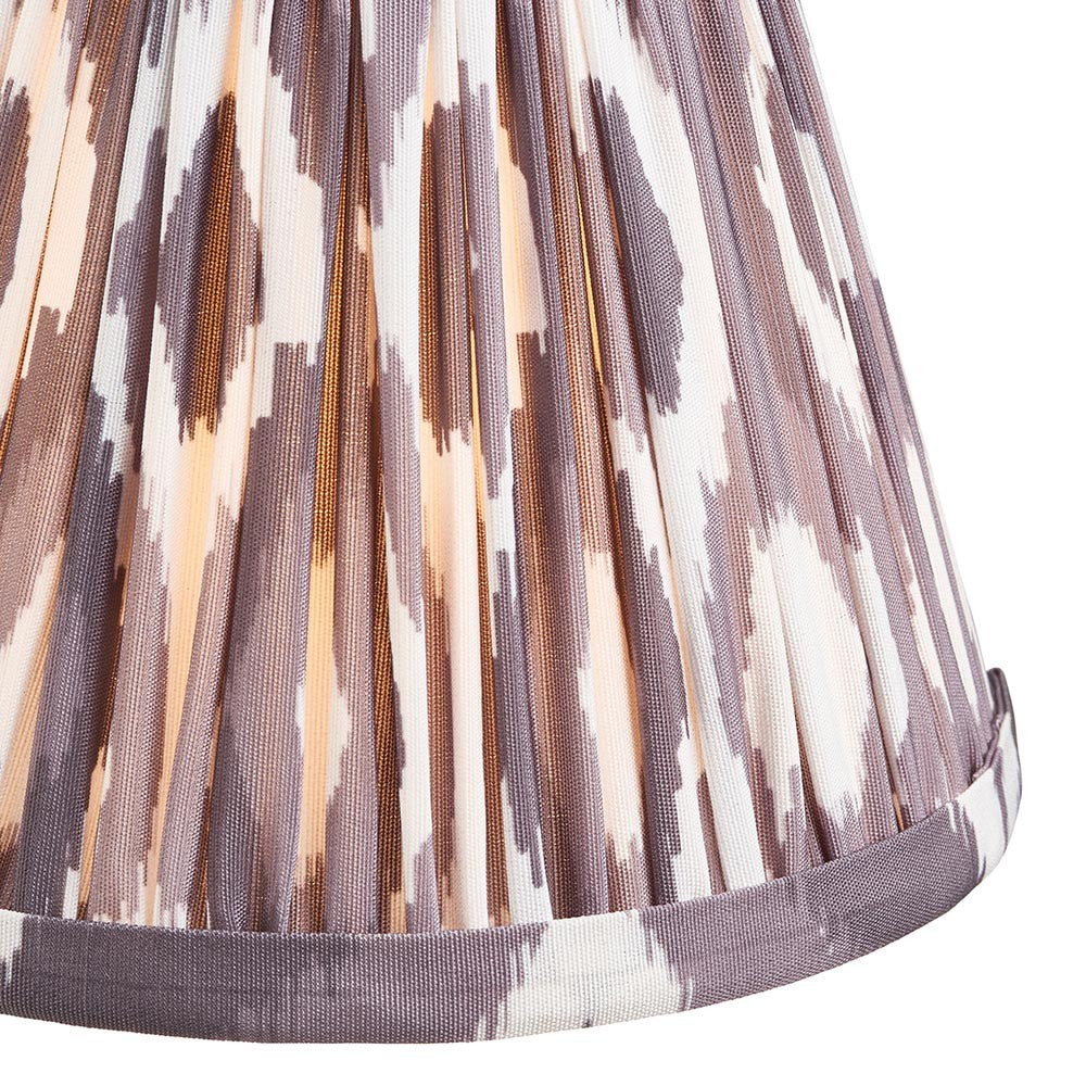 Endon Brenwell 16cm tapered lamp shade in pearl grey pleated faux silk with an ikat print and taped edge trim, shown illuminated in close-up.