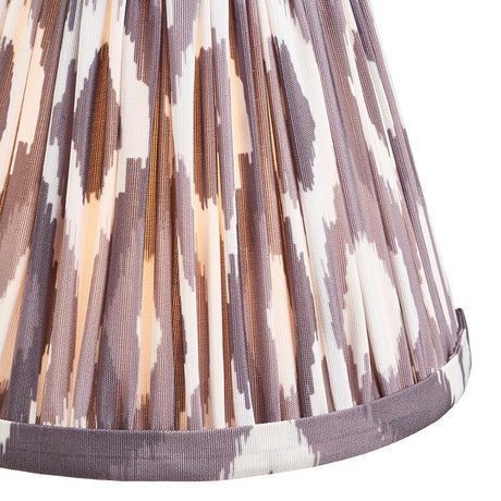 Endon Brenwell 16cm tapered lamp shade in pearl grey pleated faux silk with an ikat print and taped edge trim, shown illuminated in close-up.