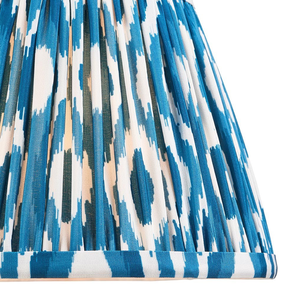 Close-up of Endon Brenwell 20cm tapered lamp shade in marlin blue, showing pleated faux silk with ikat pattern in blue, white and green tones.