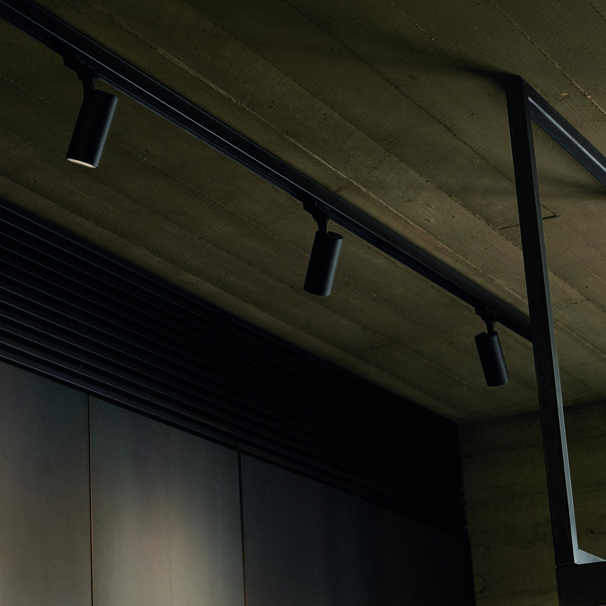 Brillia 1m black surface-mounted lighting track fitted to a ceiling, shown with three cylindrical spotlights attached along its slim rectangular rail.