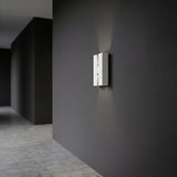 Briscola LED Outdoor Wall Light in white steel, a slim rectangular fixture with a narrow central slot, mounted on a dark wall and casting upward and downward light beams.