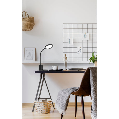 Brolini black LED touch table lamp with round flat head and flexible gooseneck on a home office desk, shown beside a mug, notebooks and wall grid board.