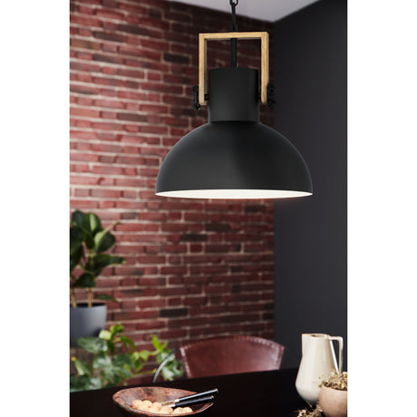Brosora Pendant Light in black steel with a deep dome shade, white interior, wood square yoke and black chain, shown above a dining table against a brick wall.