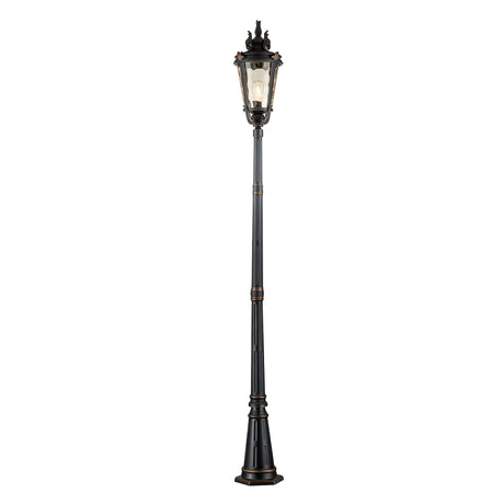 The Baltimore 1 Light Large Lamp Post - Weathered Bronze features an ornate, antique-style design with intricate detailing and amber-tinted blown glass on the lamp head. Its tall, segmented pole casts a warm glow, complemented by decorative elements at the top. The weathered bronze patina adds charm to its wide, slightly flared base.