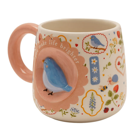 Ceramic mug in cream with a raised 3D blue bird on a pink scalloped medallion reading "you make life brighter," pink handle, and wildflower, heart and ladybird prints, on a white background.