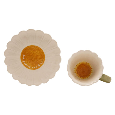 Daisy Gloss Stoneware Teacup and Saucer Set in white, shown from above with scalloped petal edges and yellow centres, plus a green handle, on a plain white background.