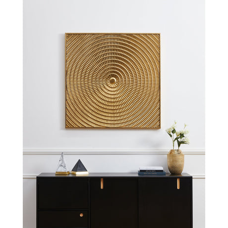 Bugrino Wall Decoration in gold, a square metal panel with slim border and raised concentric ribbed rings radiating from a central boss, displayed above a black sideboard.