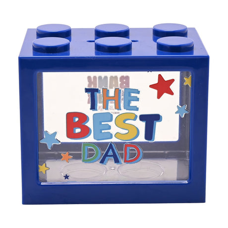 Navy blue brick-shaped plastic money box with six studs, a clear front window printed "THE BEST DAD" in colourful letters with star accents, on a white background.