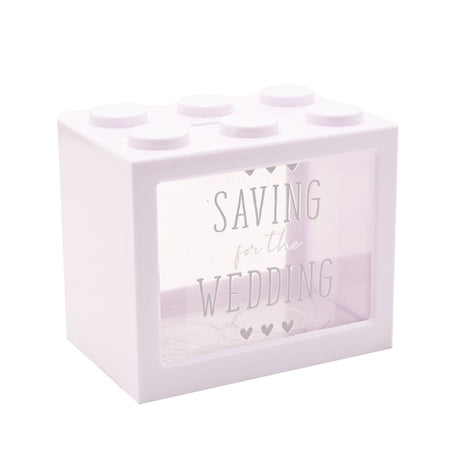 White plastic building block money box with six top studs and a clear front panel reading "Saving for the Wedding" in grey capitals with hearts, shown on a plain background.