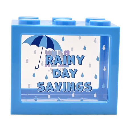 Blue plastic building block money box with six round studs, clear front window printed with "Rainy Day Savings" and an umbrella and raindrop design, on a white background.