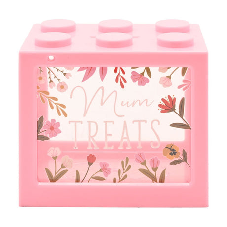 Pink plastic brick-shaped money box with six round studs on top and a clear front window reading "Mum TREATS", framed by illustrated pink, coral and green florals, on a white background.