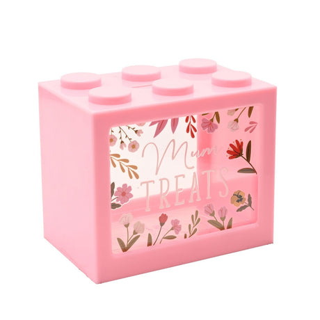 Pink plastic building brick-shaped money box with six top studs and a clear front window printed "Mum Treats", framed by illustrated pink and coral florals, on a plain white background.