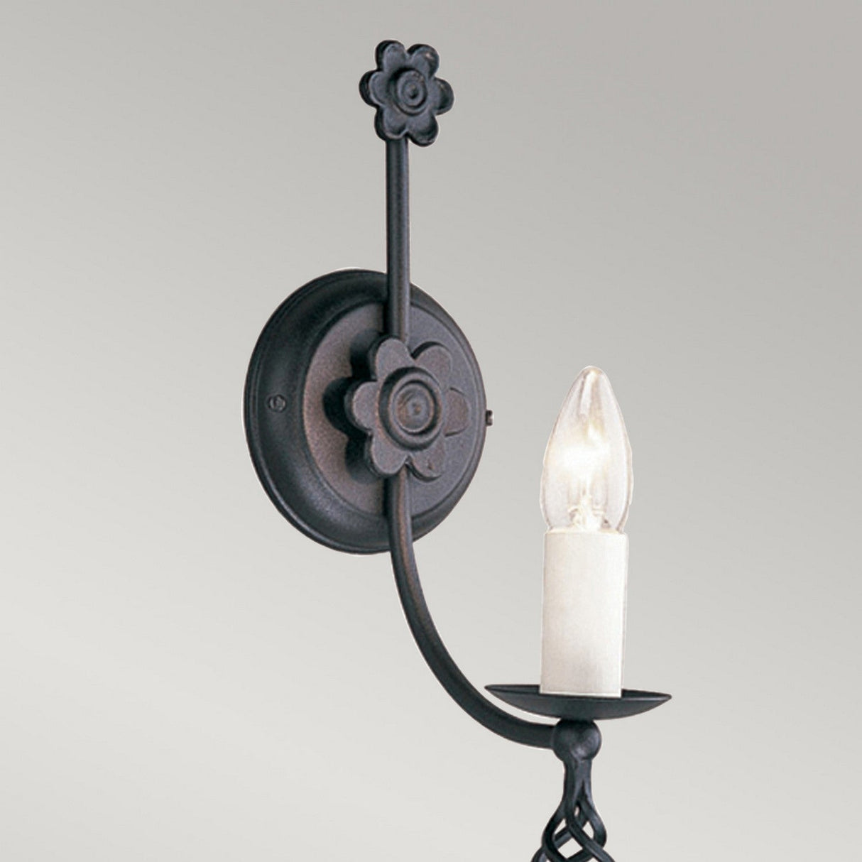 The Belfry 1 Light Wall Light in black features an ornate metal design with old-world charm and a floral pattern, holding a single candle-shaped light bulb, and is mounted on a round base against a neutral background.