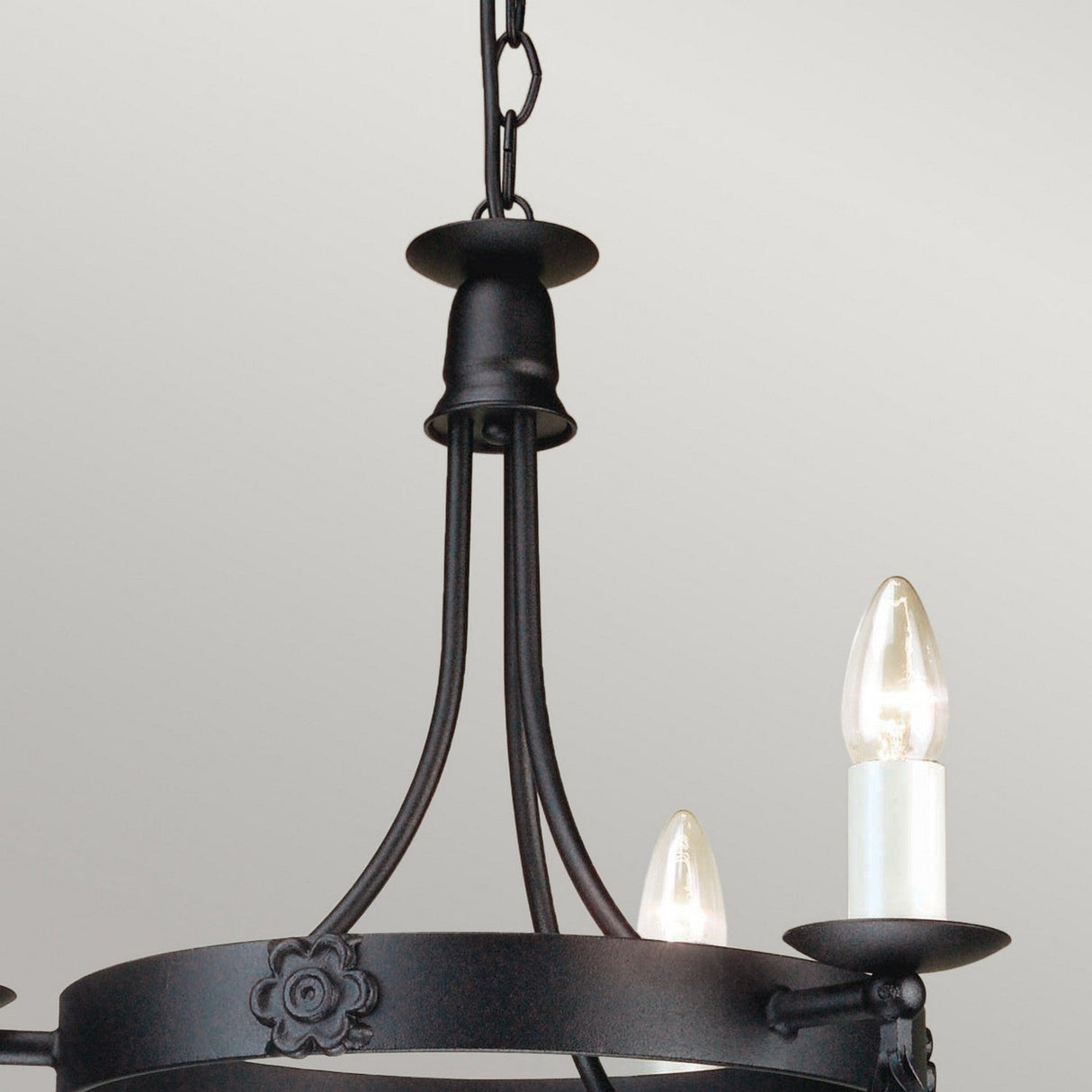Close-up of the Belfry 3 Light Chandelier - Black highlighting its medieval craftsmanship. This chandelier, constructed from black wrought iron with a hand-forged metal frame and decorative floral accents, features two candle-shaped bulbs set against a light gray background.