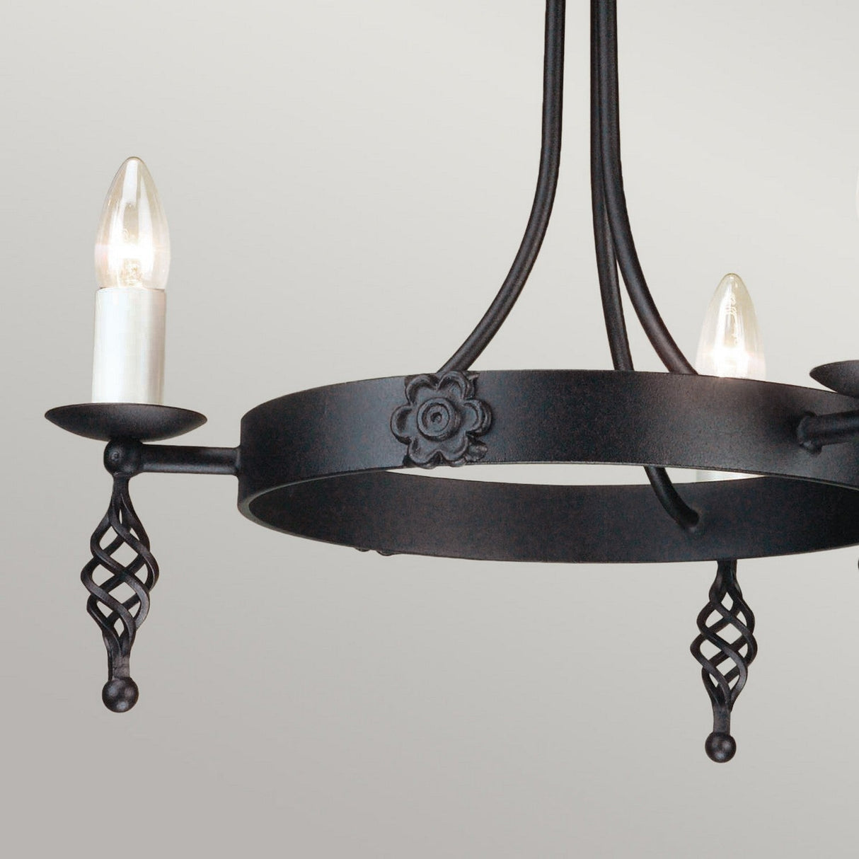 The Belfry 3 Light Chandelier - Black features a circular base with two lit candle-style bulbs. Displaying medieval craftsmanship, it is adorned with intricate floral designs and twisted metal accents on its hand-forged metal frame, standing elegantly against a plain neutral background.