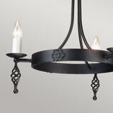 The Belfry 3 Light Chandelier - Black features a circular base with two lit candle-style bulbs. Displaying medieval craftsmanship, it is adorned with intricate floral designs and twisted metal accents on its hand-forged metal frame, standing elegantly against a plain neutral background.