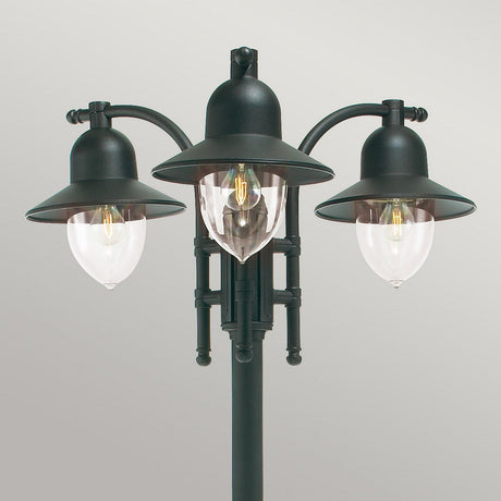 The Como 3 Light Triple Head Post - Black, designed for durable outdoor lighting with its IP54 rating, boasts black metal fixtures and clear glass shades that elegantly display an exposed filament bulb against a neutral backdrop.