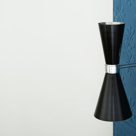 Cairo Cone Twin Wall Light in gloss black with chrome collar and arm, hourglass double-cone shade mounted on a textured blue panel against a white wall.