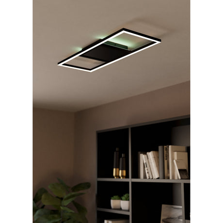 Calagrano Smart LED Flush Ceiling Light in black aluminium and steel, open rectangular frame with offset panel, shown glowing on a bedroom ceiling above a dark bookshelf.