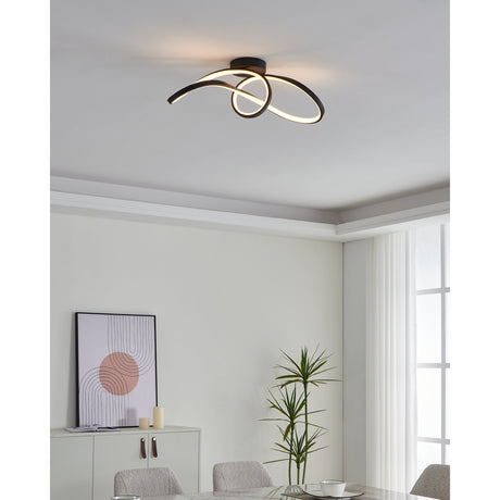 Calarossa Smart Colour Changing LED Ceiling Light in black, a looped ribbon-style flush fitting with integrated warm LED glow, shown on a white ceiling above a dining area.